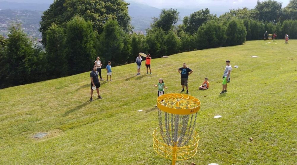 Jugadores de disc golf disfrutando del juego en un campo con pendiente y canasta amarilla