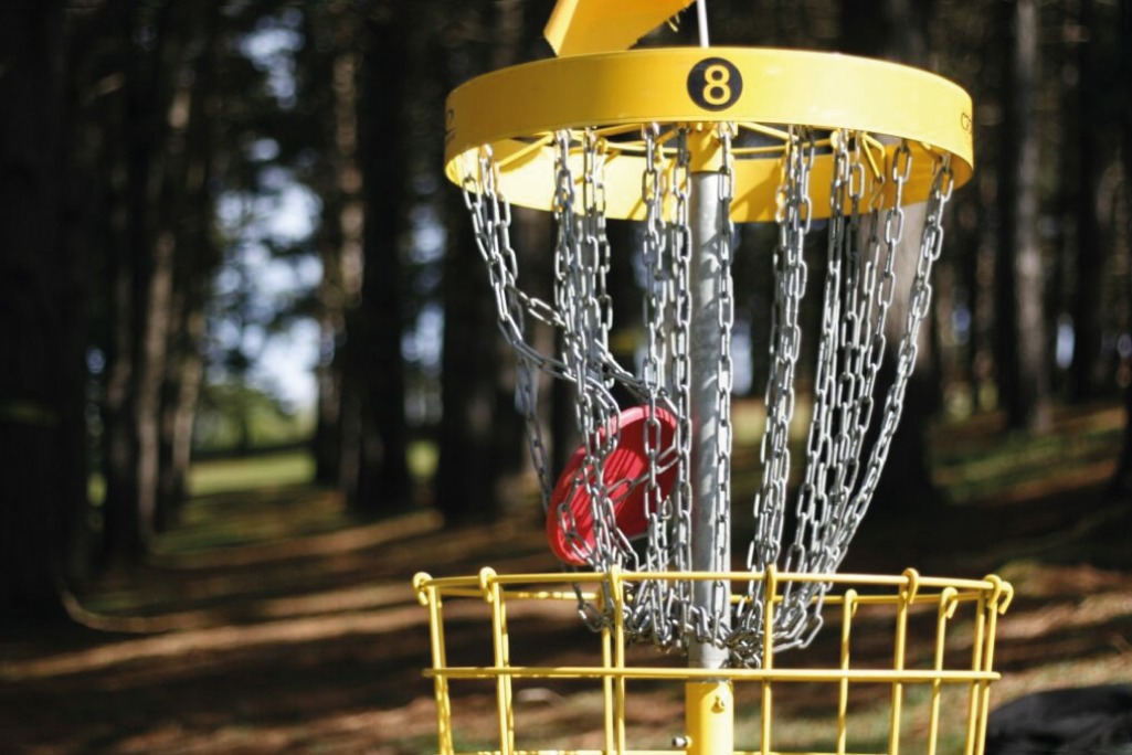 Disco rojo de disc golf entrando en una canasta amarilla numerada en un bosque