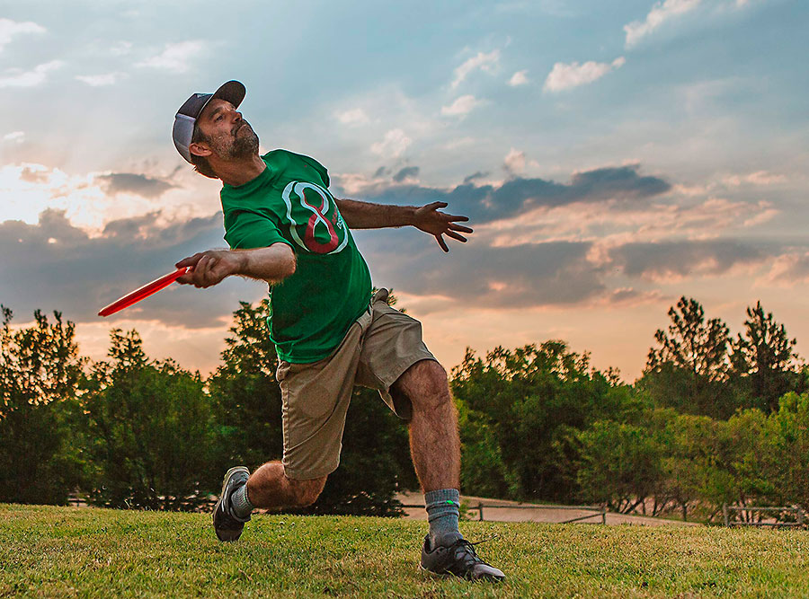 Jugador lanzando un disco de disc golf en un campo abierto al atardecer