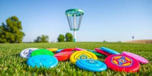 Discos de disc golf de colores colocados sobre césped con una canasta al fondo
