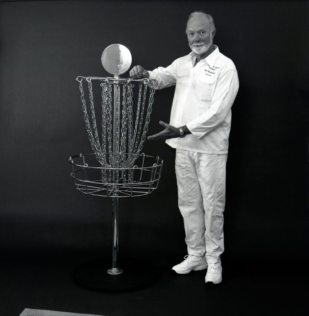 Hombre mayor mostrando la primera canasta oficial de disc golf en fondo negro